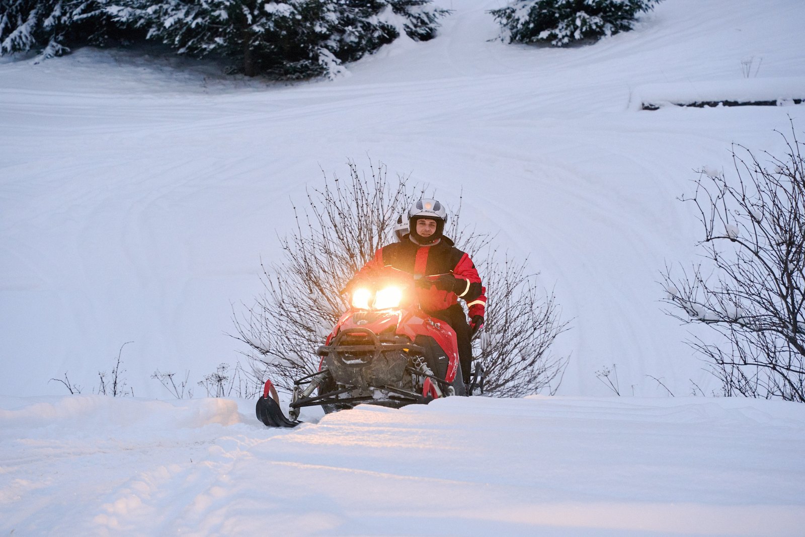 Snowmobile with its headlight on at dusk in a snow-covered forest - the MOON tour